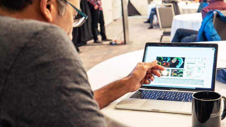 Researcher seated at a table analyzing data on a laptop