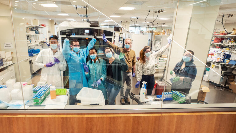 Laboratory team raising their hands and cheering from behind a window