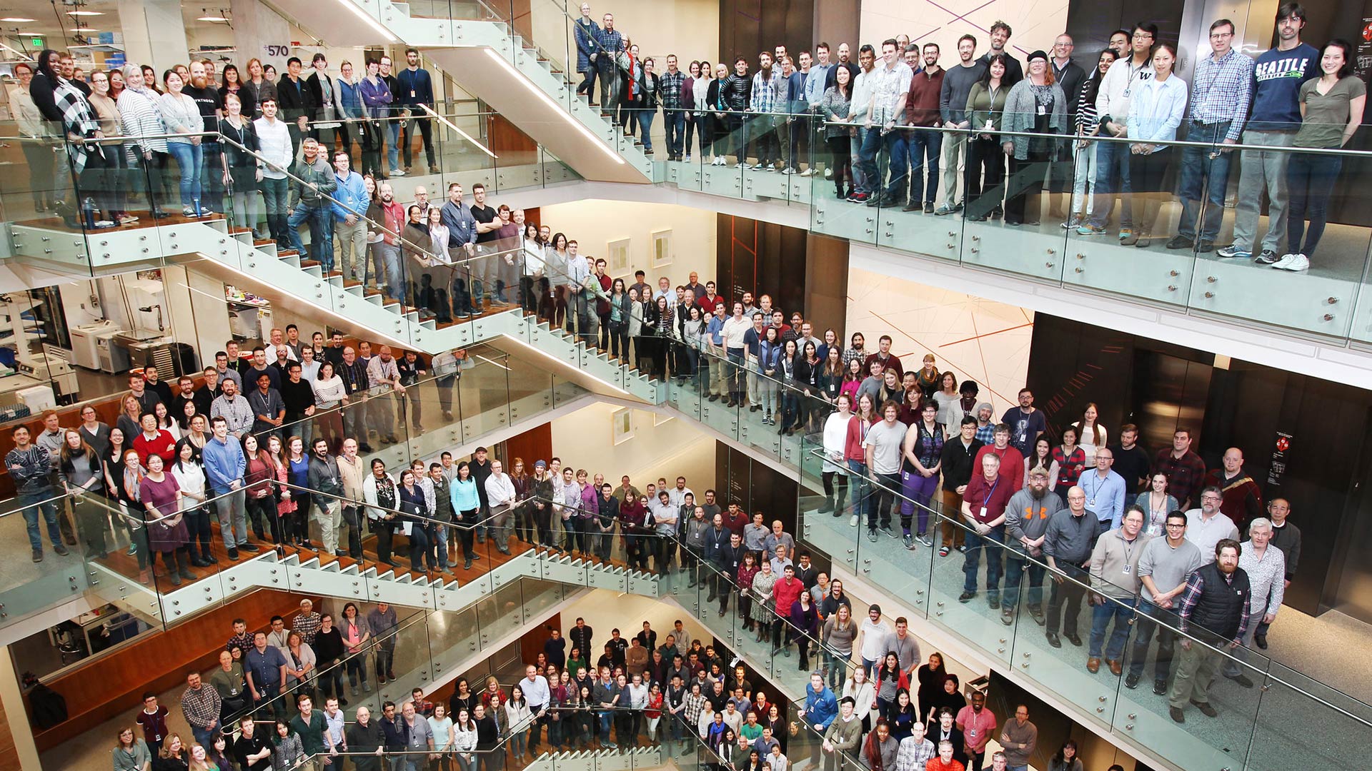 Hundreds of men and women standing in the halls and staircases of the Allen Institute posing for an all-staff photo