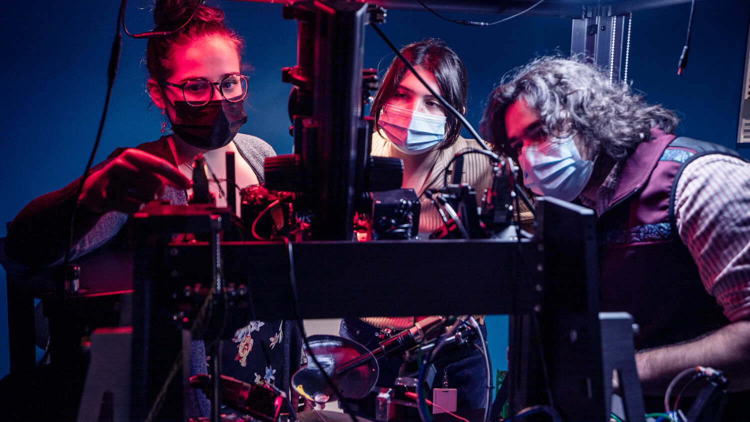 Allen Institute neuroscientists (from left to right) Tamina Ramirez, Hannah Cabasco and Henry Loeffler examine equipment on the Neuropixels rig, a specialized piece of equipment that allows OpenScope scientists to capture electical activity of hundreds to thousands of neurons in a single experiment.