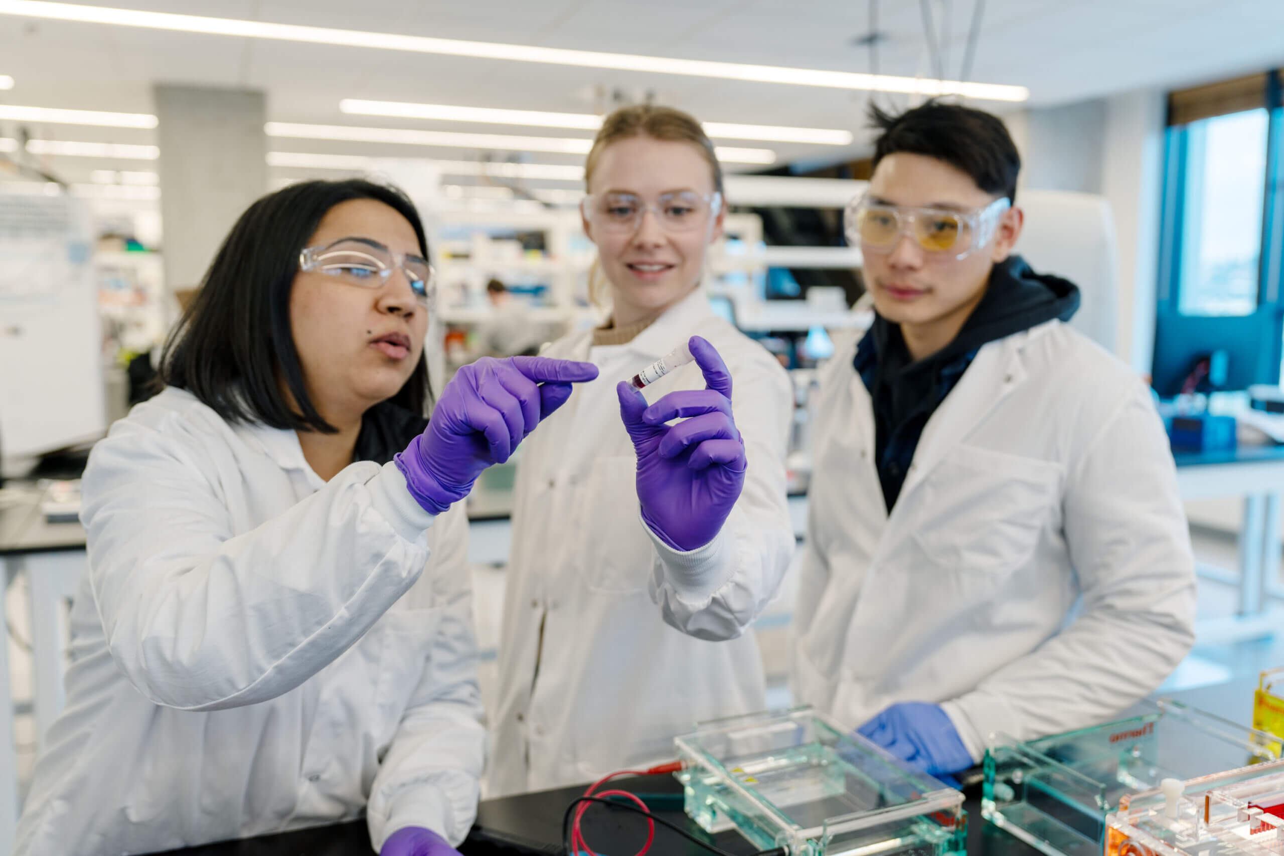 Three researchers dressed in which lab coats examining a sample slide