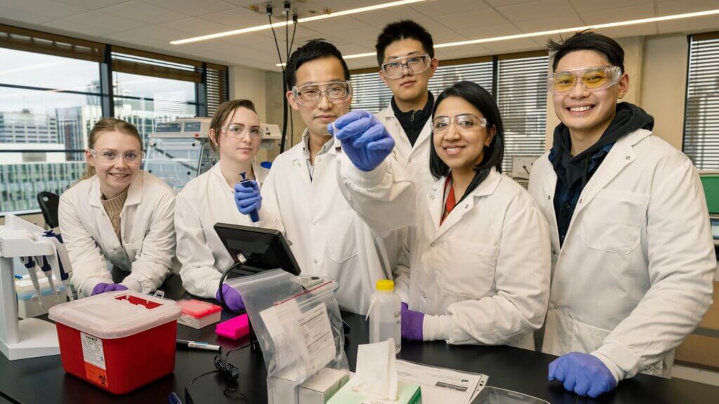A group of 6 researchers in lab coats posing for a group photo in the lab