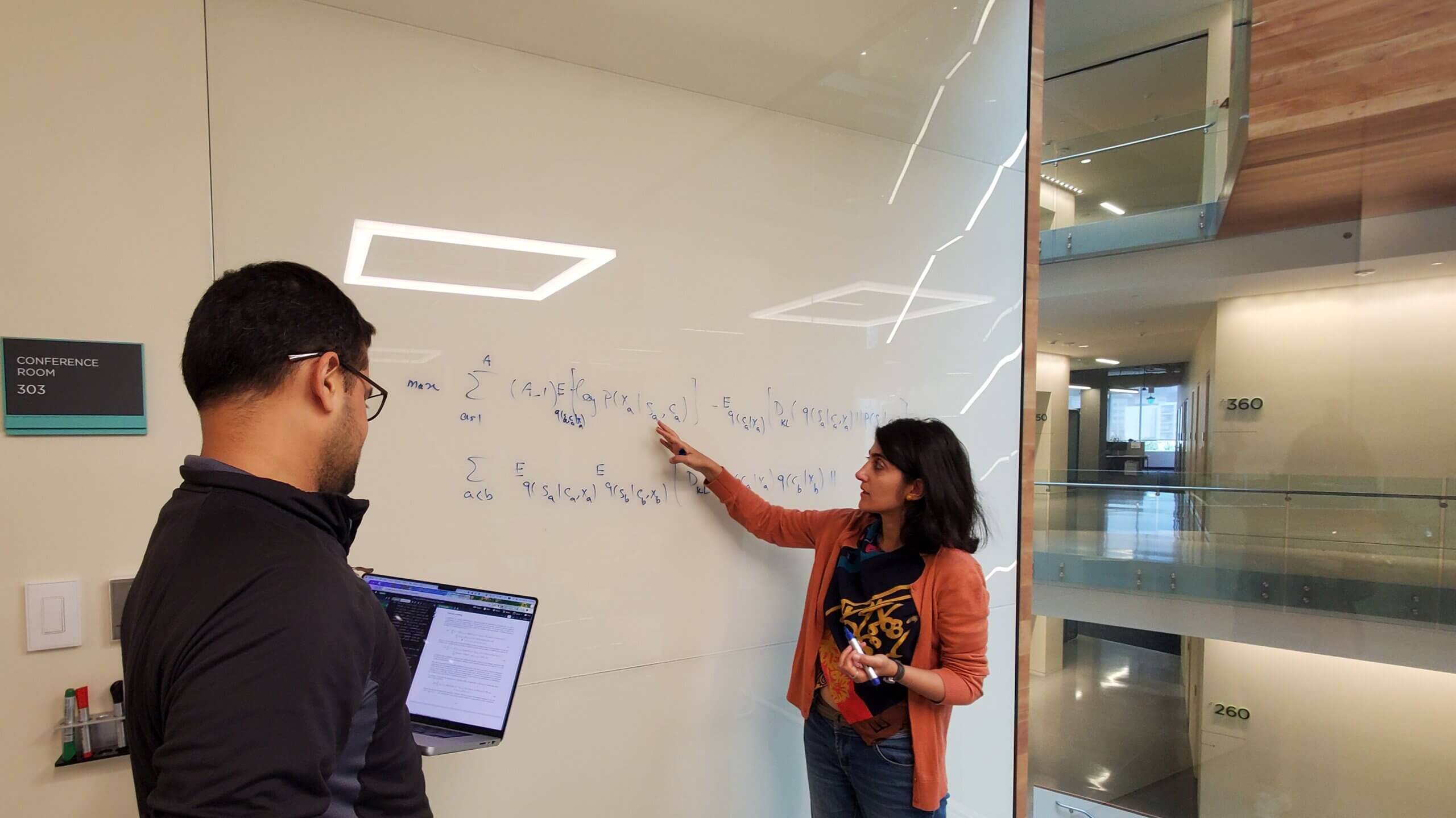 Two scientists stand in front of a whiteboard with an equation