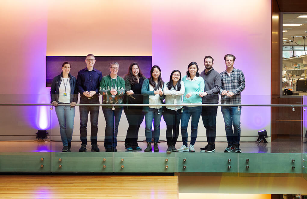 Photo of multiple individuals standing outside a lab with colorful lights as a background.