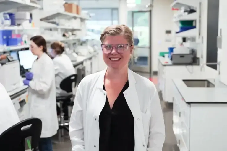 A female scientist smiles in front of a laboratory background