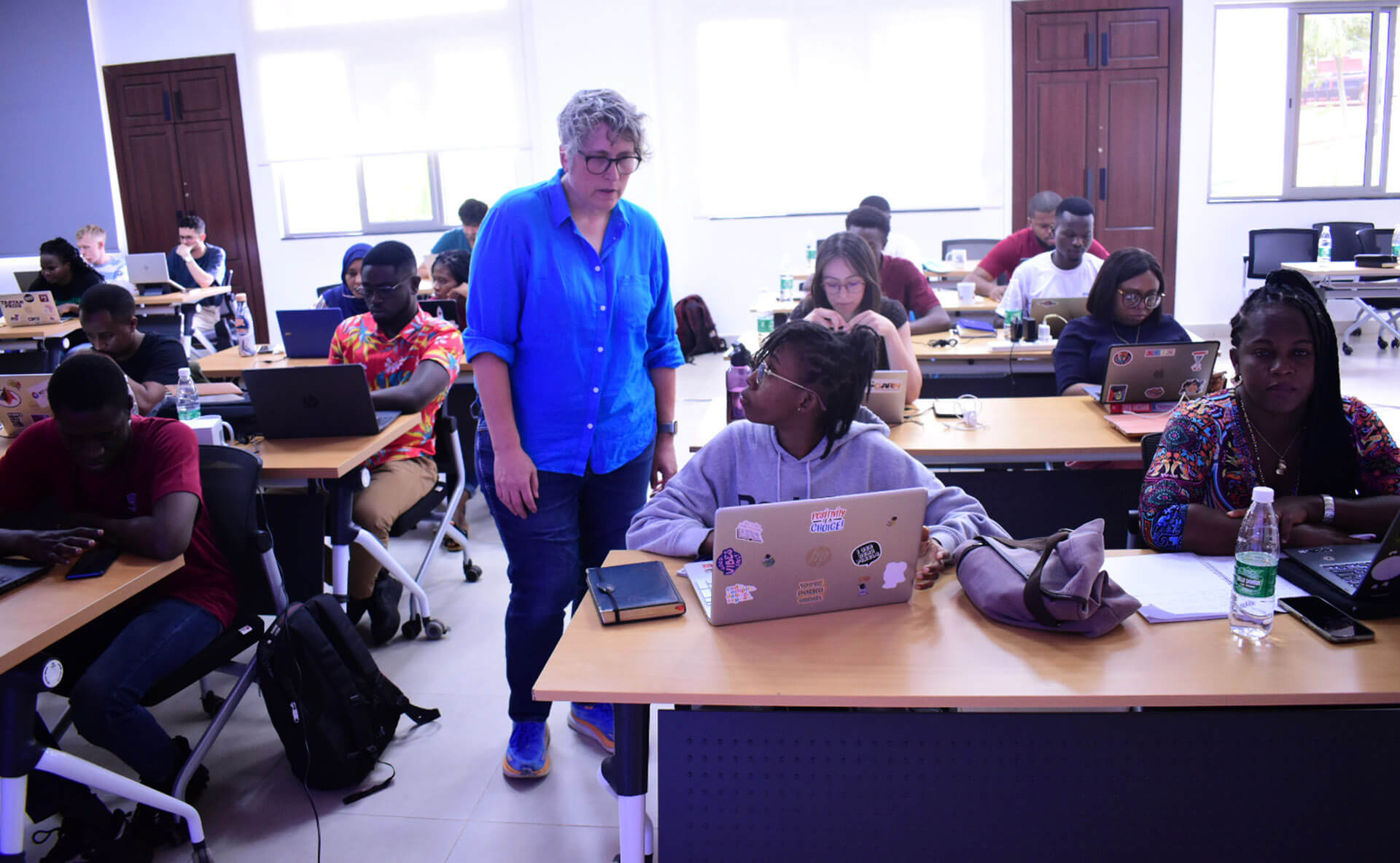 A woman in a blue shirt standing over a student at a desk