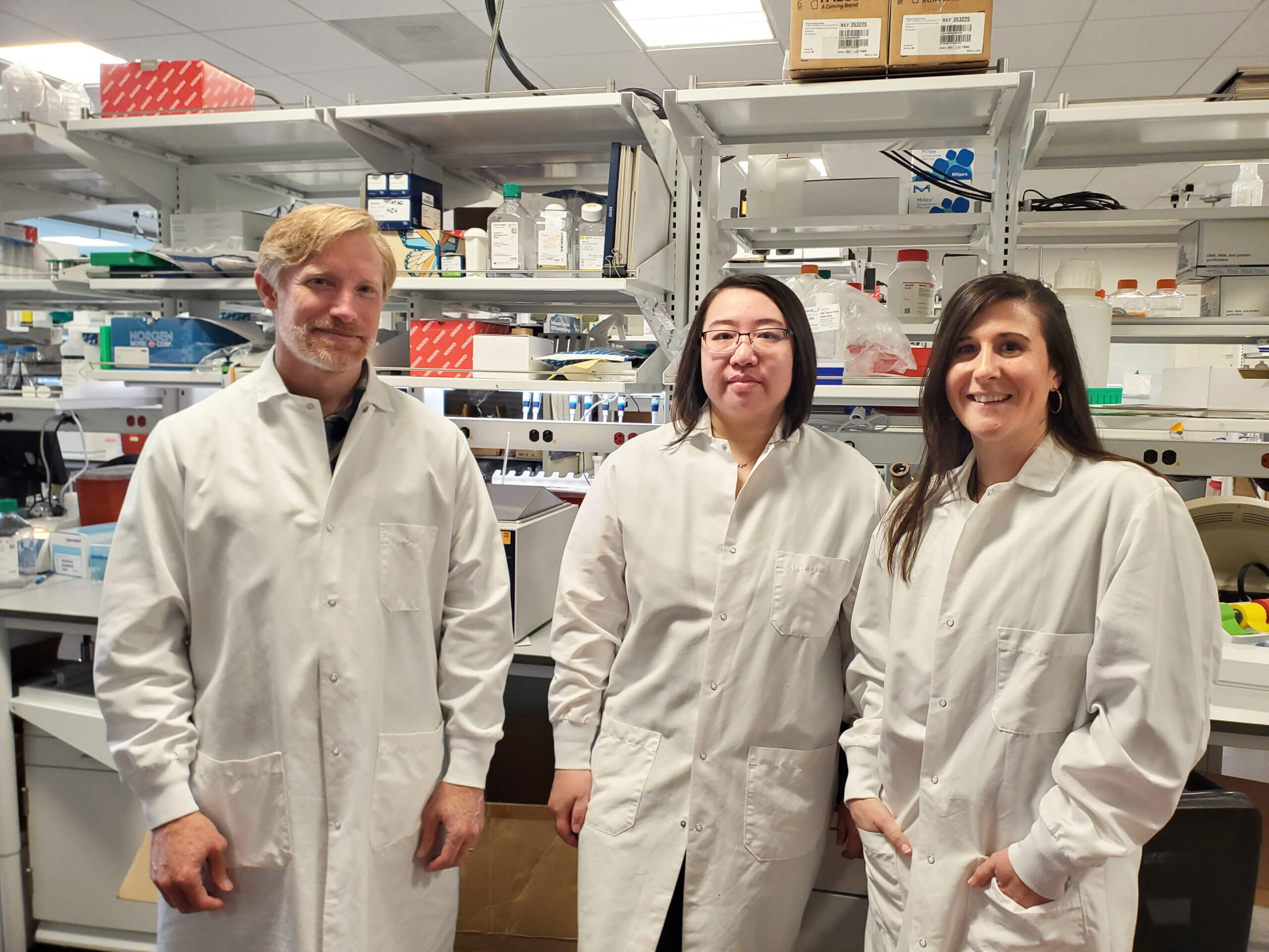 Three researchers wearing lab coats posing for a photo in a laboratory