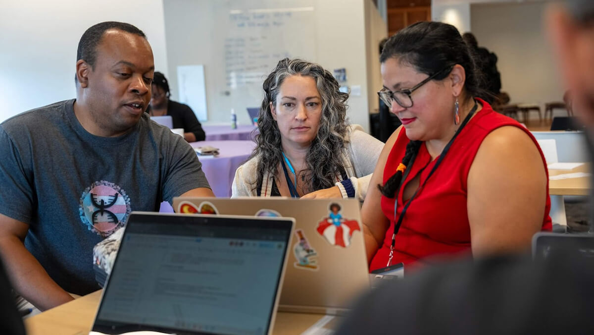 3 scientists/educators sit around a laptop